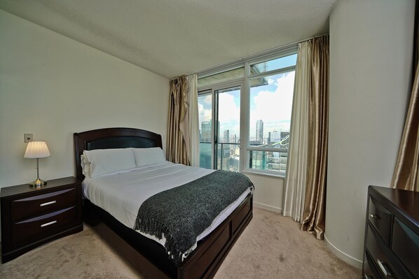 A bedroom with a large bed, a nightstand, a dresser, and a window with curtains. - Delsuites Toronto (Toronto)