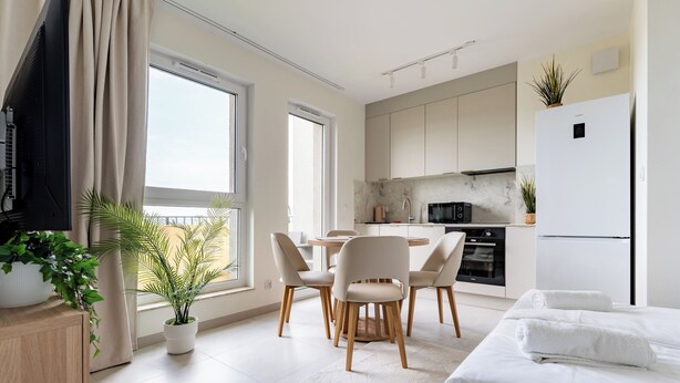 A modern hotel room with a bed, a dining area with chairs, a kitchen with cabinets, and a large window. - Rumia Stylish Apartment (Rumia)