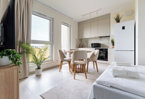 Quarto de hotel moderno com cama, área de jantar com cadeiras, cozinha com armários e uma janela grande.