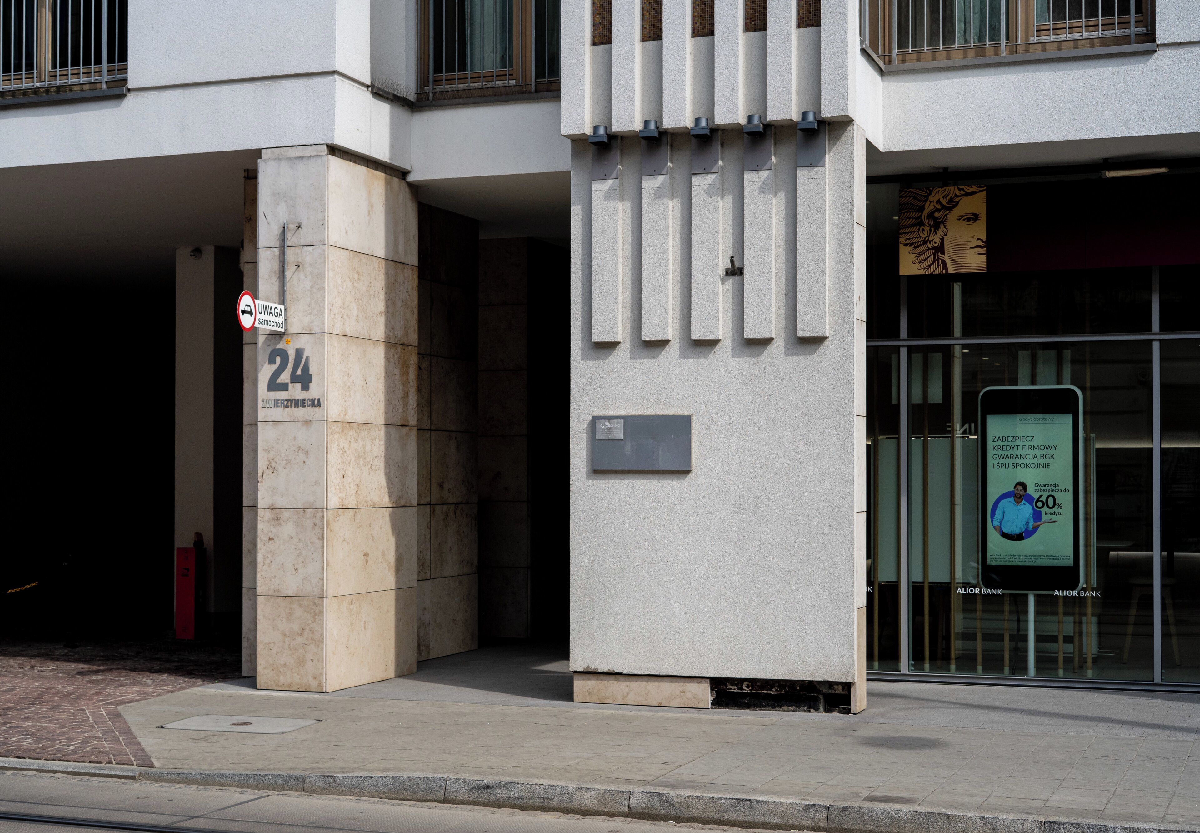 Ein Gebäudeeingang mit einem Schild, das '24' anzeigt, und einem Verbotsschild für Fahrzeuge.