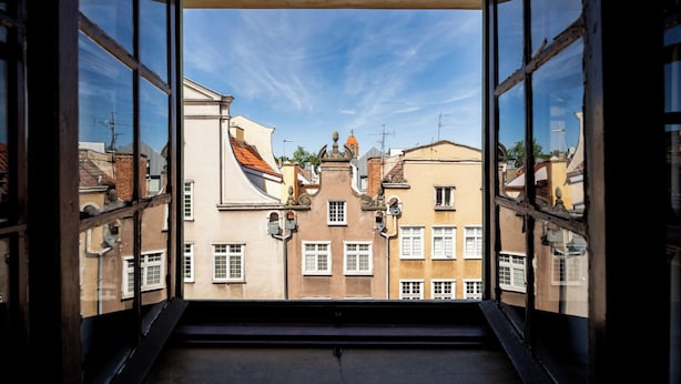 A view through a window with a clear sky, buildings with distinct architectural styles, and a visible chimney. - Heart of Gdańsk Mariacka Apartment (Gdańsk)