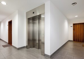 A hallway with an elevator, a wooden door, and a tiled floor. - Giełdowa Lavish Apartment (Warszawa)