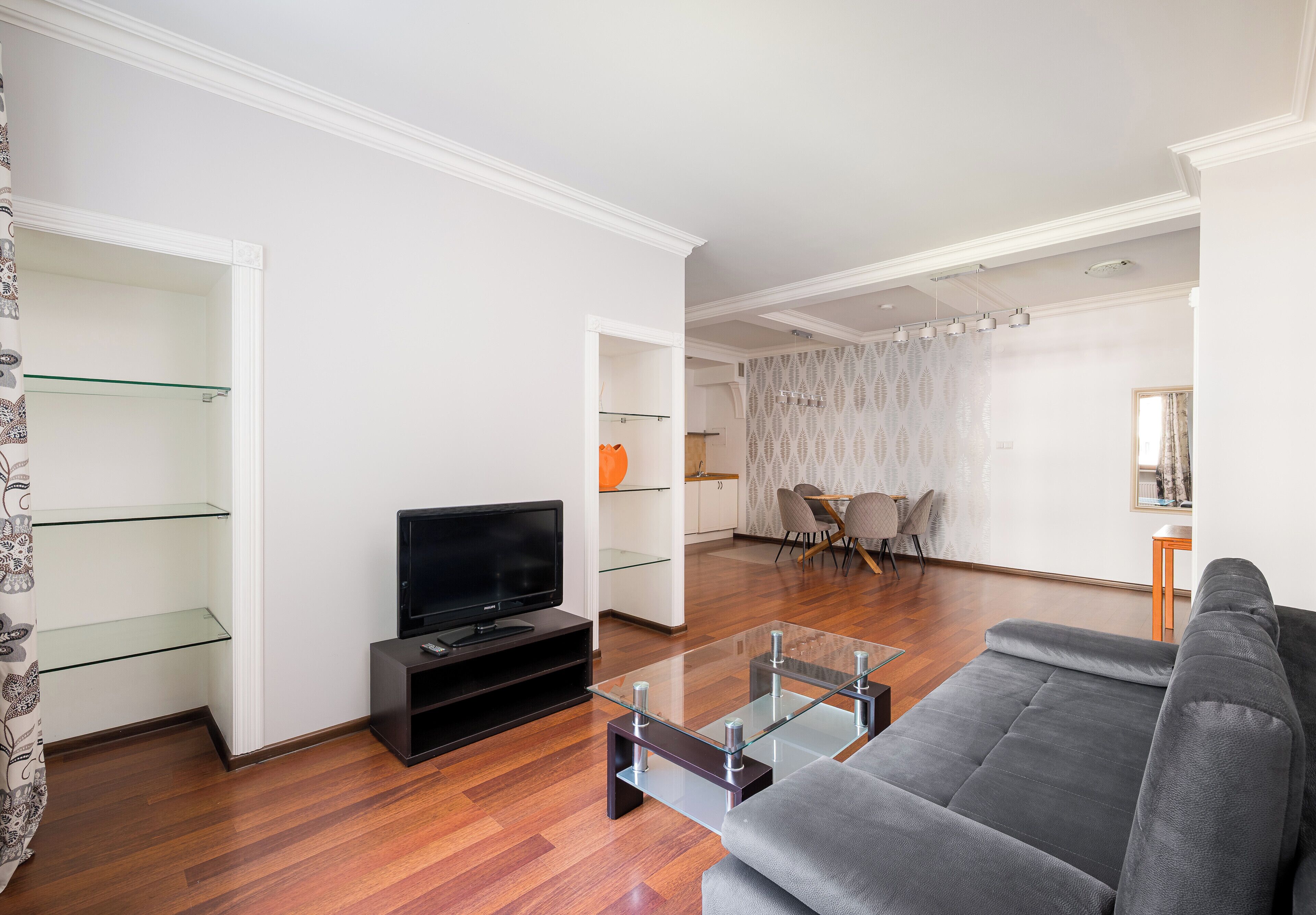 A modern living room with a flat-screen TV, a glass coffee table, and a grey sofa.