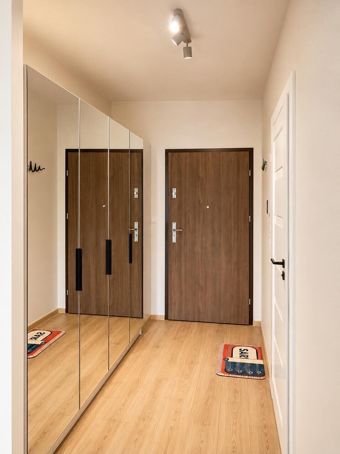 Un pasillo con suelo de madera, un armario espejado y una puerta con manija.