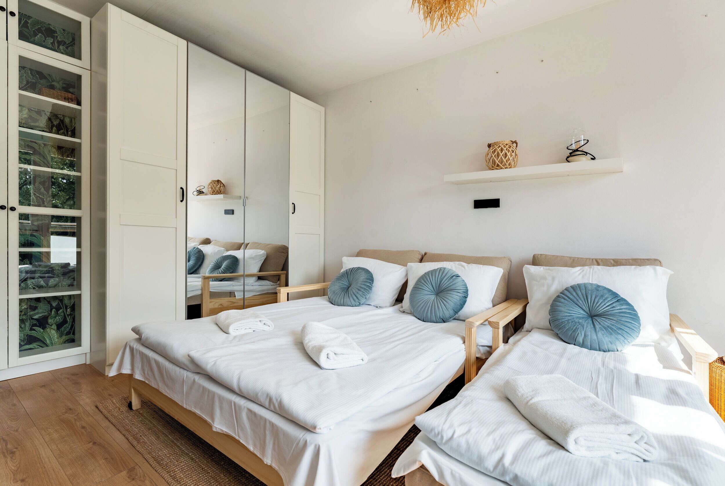 A bedroom with two beds, a wardrobe, a shelf with decorative items, and a mirror.