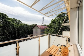 Un balcon avec une table en bois, un panier en osier et une vue sur une maison et des arbres.