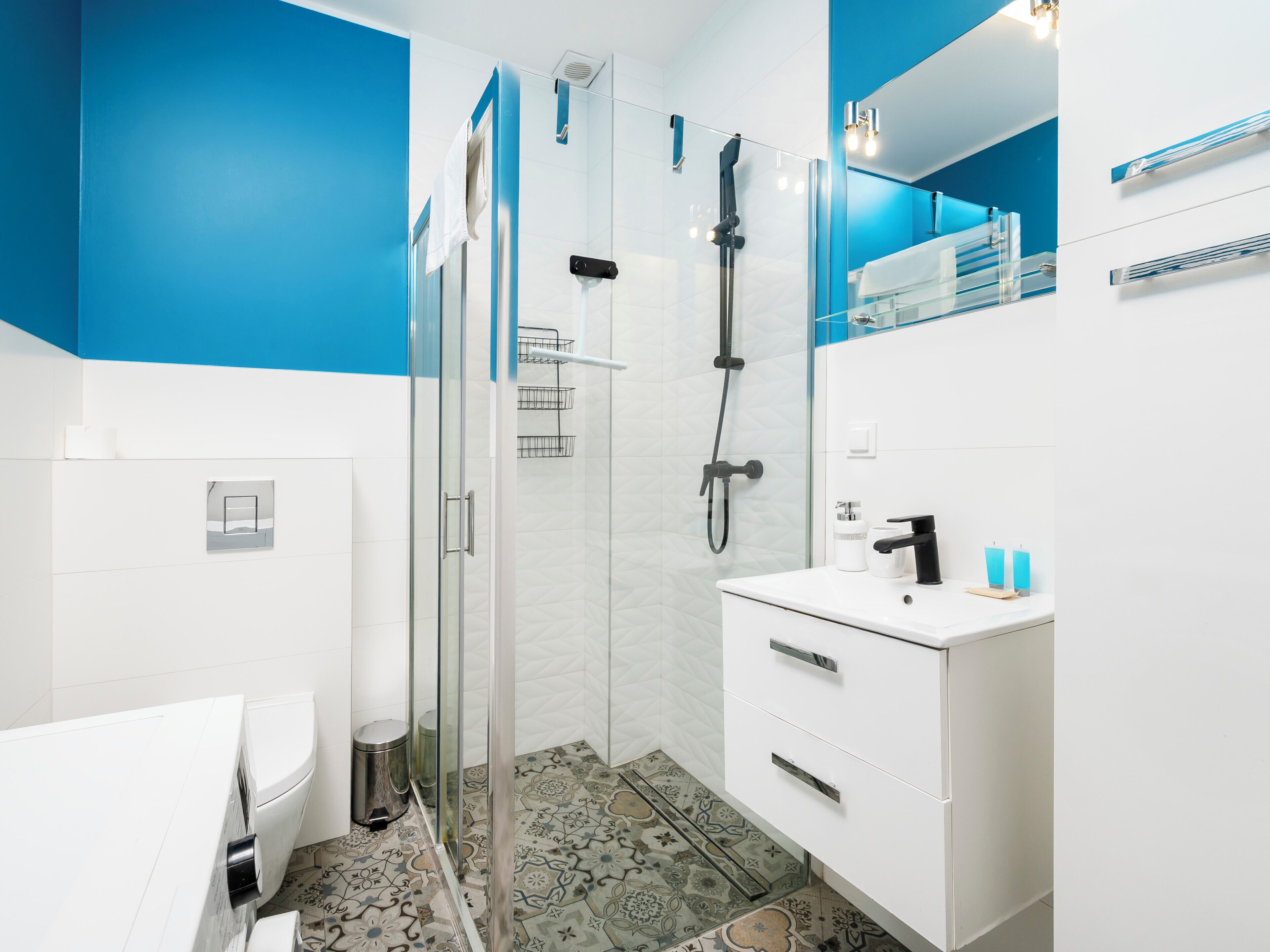 A modern bathroom with a glass shower enclosure, a white sink with a mirror, and patterned floor tiles.
