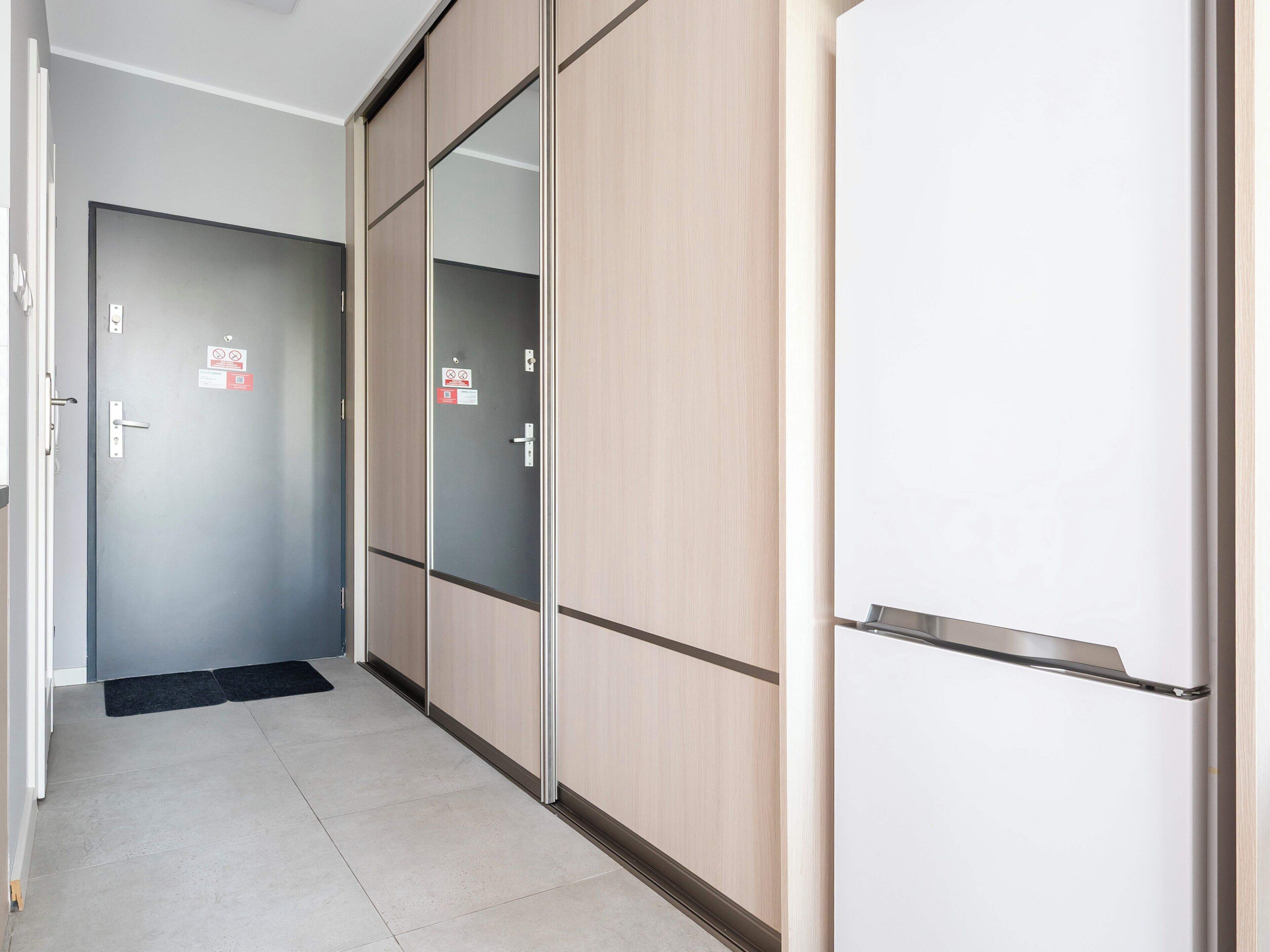A hallway with a door, a refrigerator, and a black mat.