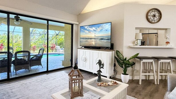 A spacious living area with a large TV, a dining table, and a view of a pool. - Golf Retreat - Pool, Spa & Fire Pit (Rotonda West)