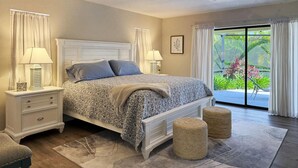 A bedroom with a bed, nightstands, a ceiling fan, and a view of greenery outside. - Golf Retreat - Pool, Spa & Fire Pit (Rotonda West)