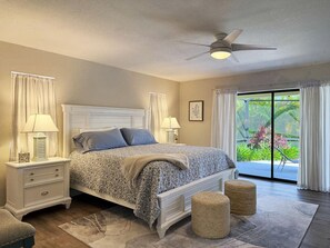 A bedroom with a bed, nightstands, a ceiling fan, and a view of greenery outside. - Golf Retreat - Pool, Spa & Fire Pit (Rotonda West)