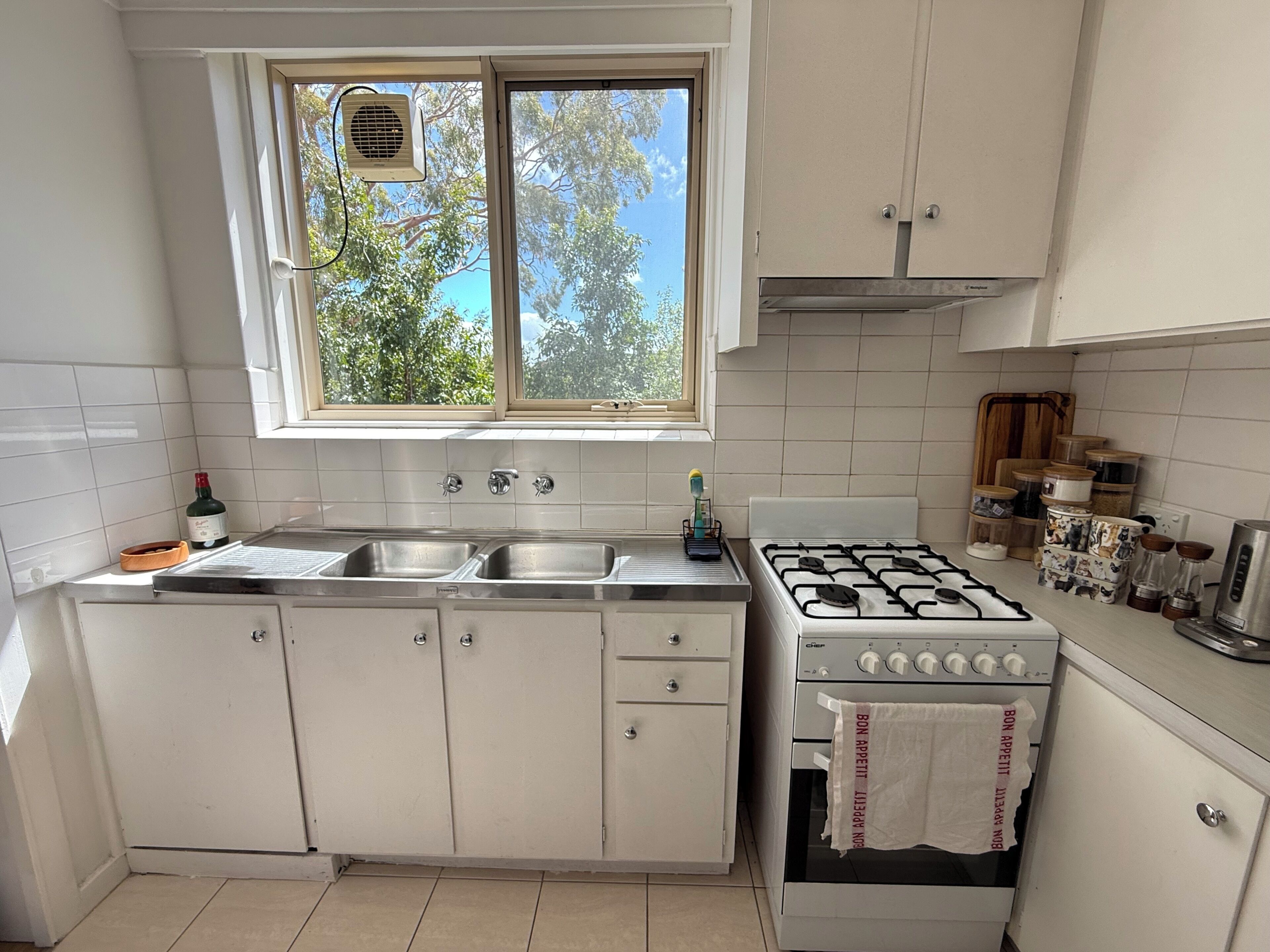 A kitchen with white cabinets, a gas stove, a sink, and a window with a view of trees.