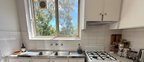 A kitchen with white cabinets, a gas stove, a sink, and a window with a view of trees.
