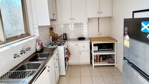 Eine kleine Küche mit weißen Schränken, einer Edelstahl-Spüle, einem Herd und einem Kühlschrank.