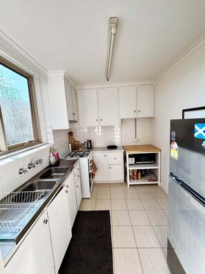 Una cucina compatta con mobili bianchi, un lavello in acciaio inossidabile, un fornello e un frigorifero.