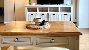 Ein Wohnzimmer mit Couchtisch aus Holz, Fernseher, Lampe, gerahmtes Bild und Korbwannen.