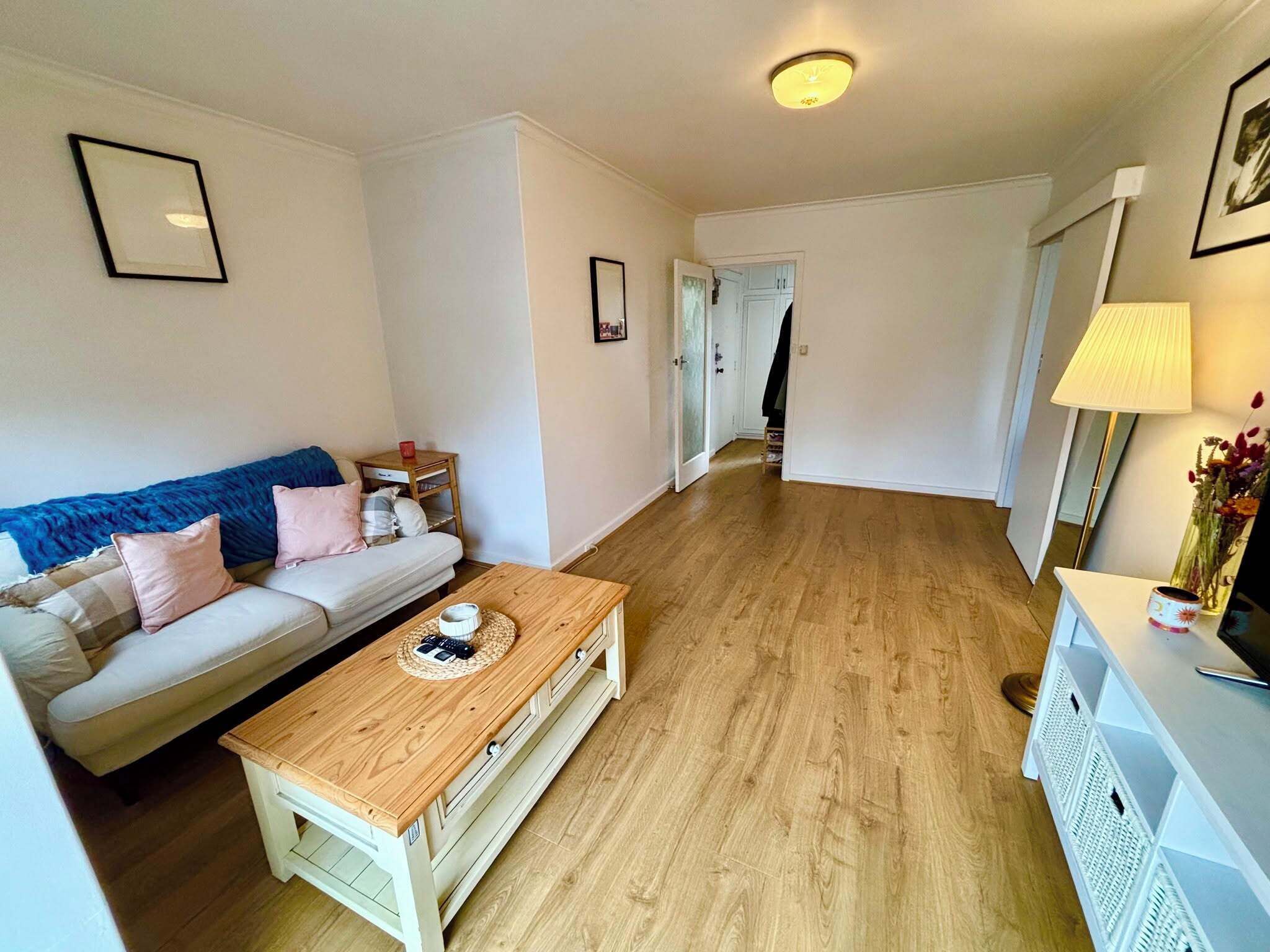 Ein Wohnzimmer mit Sofa, Couchtisch und einem zur Tür führenden Flur.