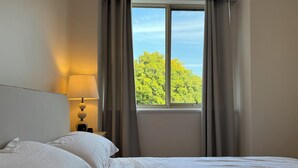 Ein Hotelzimmer mit Bett, Nachttisch, Lampe und einem Fenster mit Vorhängen.