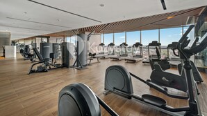 Uma academia com diversos equipamentos de ginástica, grandes janelas e piso de madeira.