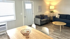 Una sala de estar con una mesa de comedor, un sofá gris y un sofá azul, además de una lámpara.