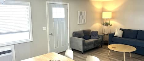 A living room with a dining table, grey sofa, blue sofa, and a lamp.