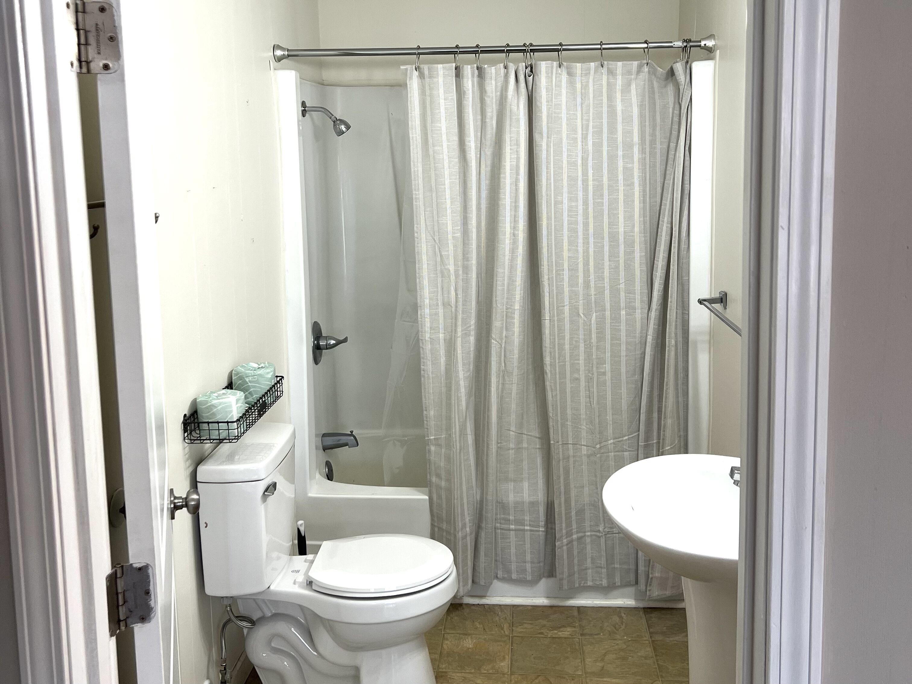 A bathroom with a toilet, a shower curtain, a bathtub, and a sink.