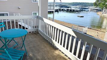 Un balcon avec une table et des chaises, donnant sur une étendue d’eau où se trouvent un quai et des bateaux.