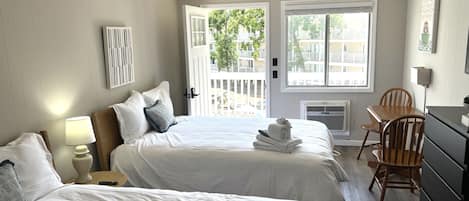 A hotel room with two beds, a desk, a chair, a dresser, and a window with a view of the outside.