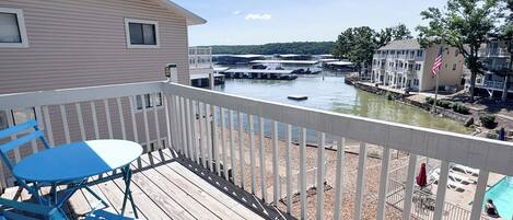 A wooden deck with a table and chairs, overlooking a marina with boats and buildings.