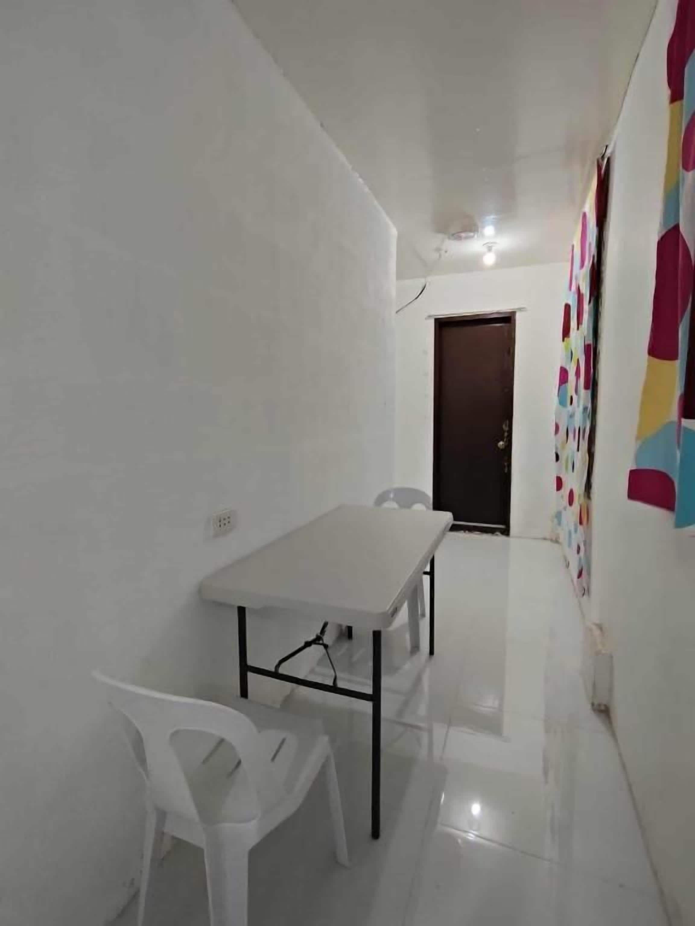 A small, clean room with a white table and two chairs, a door, and a colorful wall decoration.