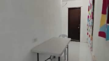 A small, clean room with a white table and two chairs, a door, and a colorful wall decoration.