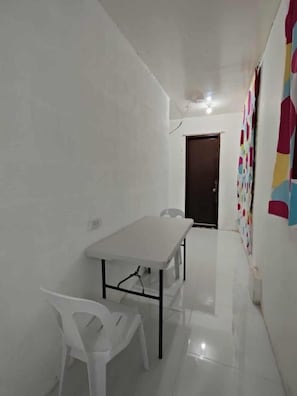 Una habitación pequeña y limpia con una mesa blanca, dos sillas, una puerta y una decoración mural colorida.