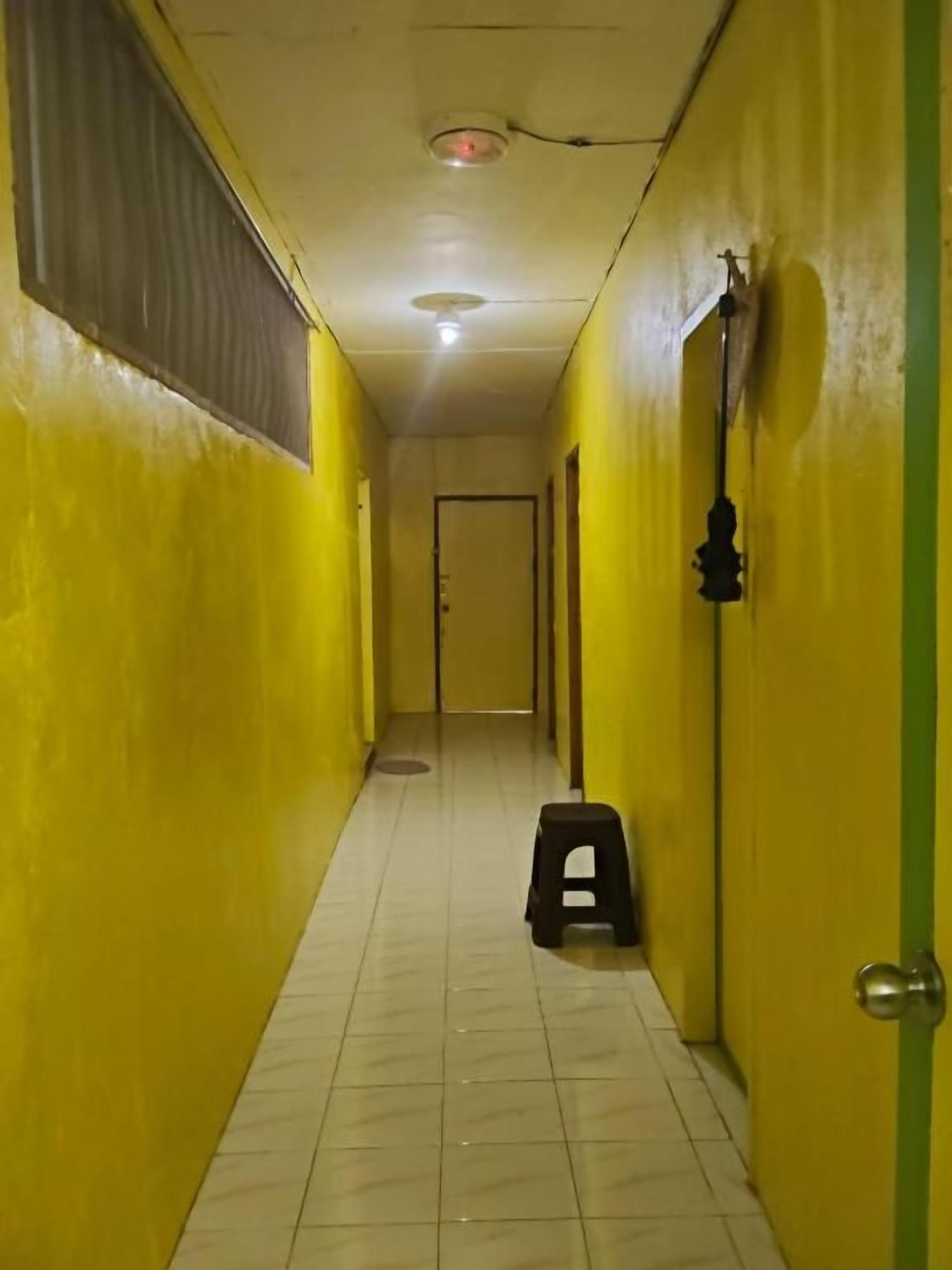 A narrow hallway with yellow walls and a tiled floor, leading to a door at the end.
