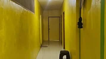 A narrow hallway with yellow walls and a tiled floor, leading to a door at the end.