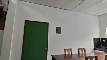 A room with a green door, a dining table with chairs, and a ceiling with visible fixtures.