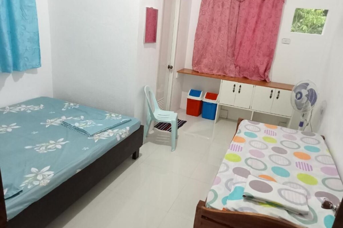 Un dormitorio con dos camas, una silla, un armario y un ventilador.