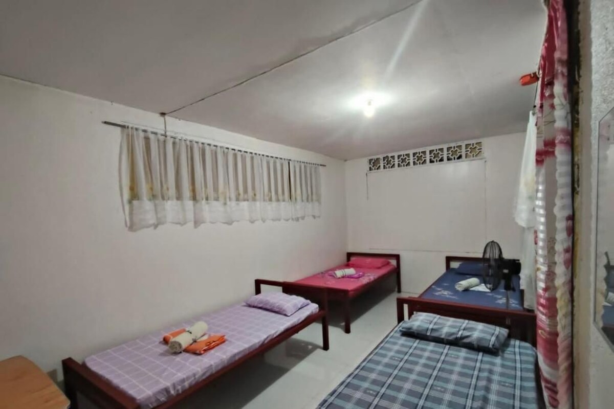A room with three single beds, a wooden table, and a ceiling light fixture.