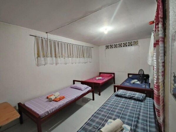 A room with three single beds, a wooden table, and a ceiling light fixture.