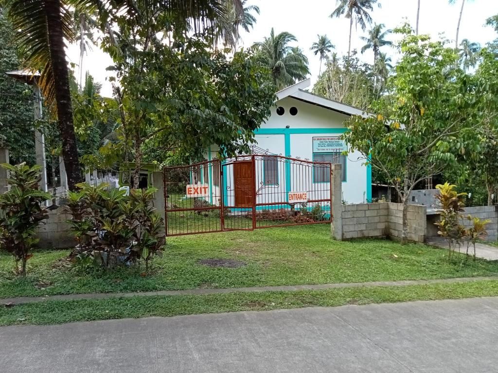 A building with a gated entrance and exit, surrounded by greenery and palm trees.