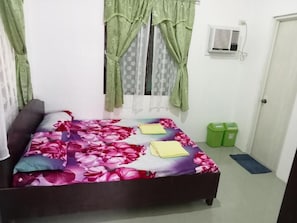 Un dormitorio con cama, cortinas, aire acondicionado, una puerta y un cubo de basura.