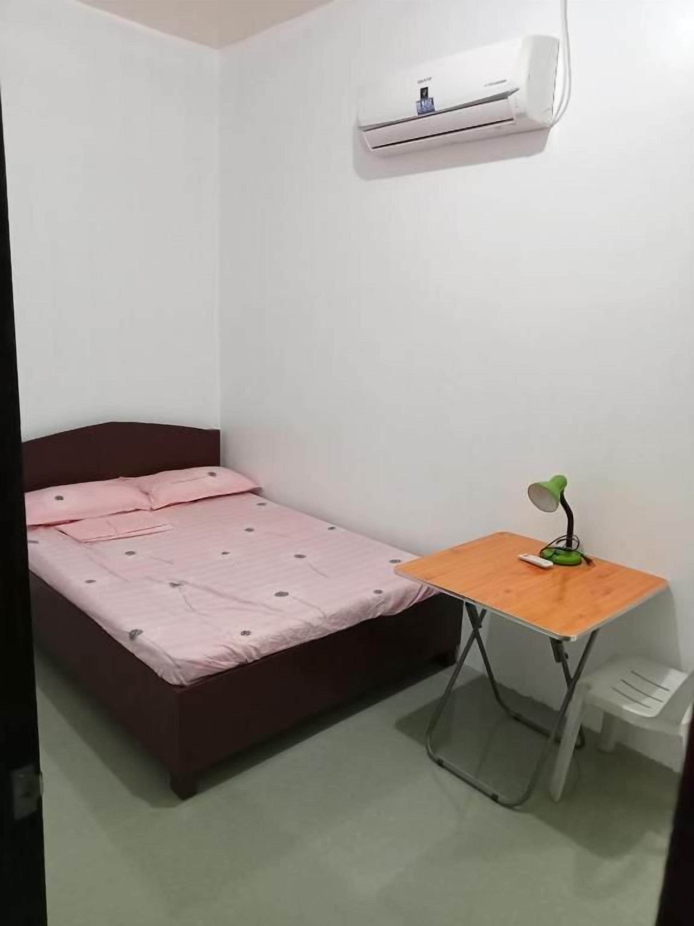 Una camera piccola con un letto singolo, una scrivania in legno e una lampada da scrivania verde.