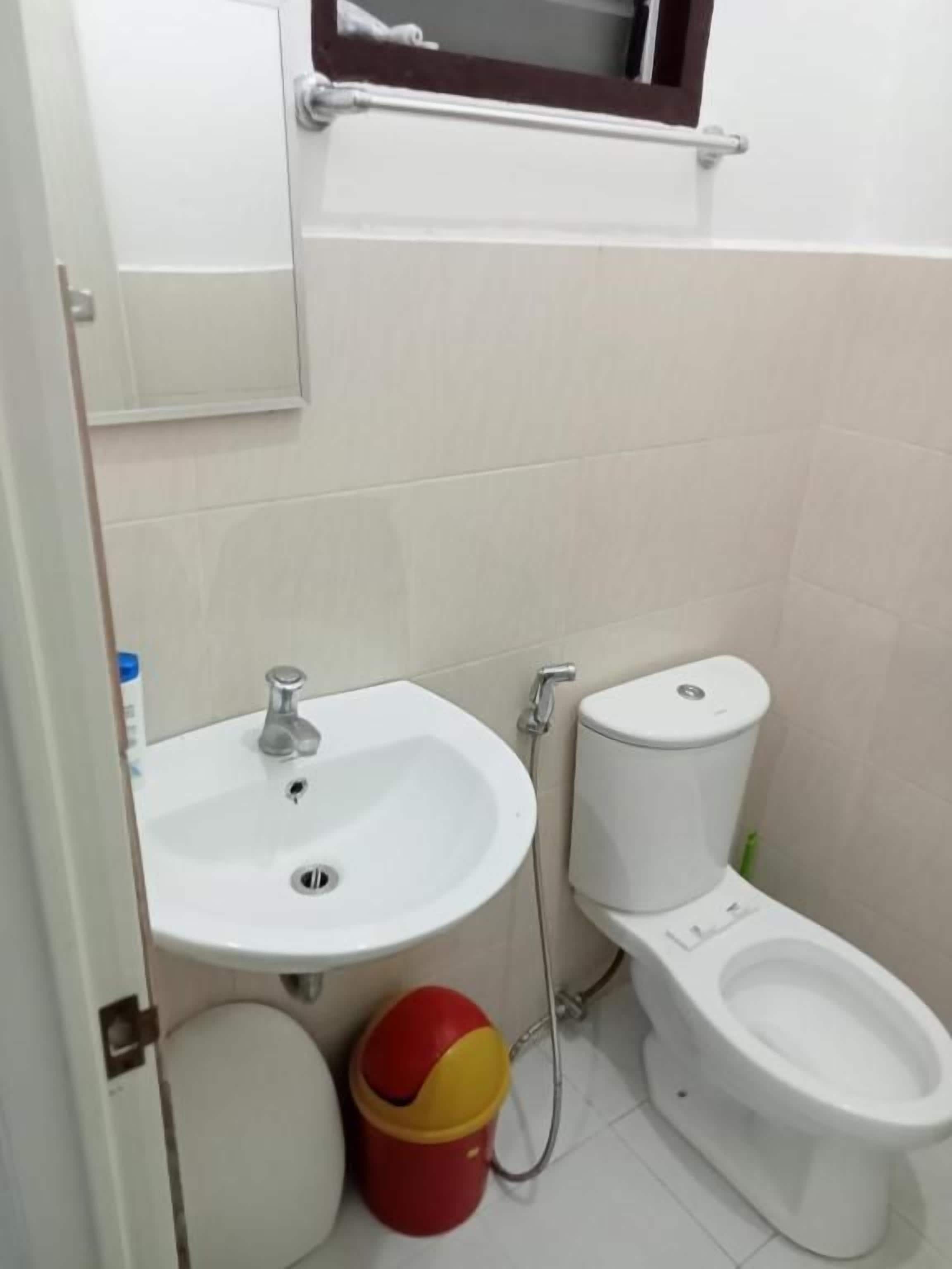 A bathroom with a sink, toilet, and a red and yellow bucket.