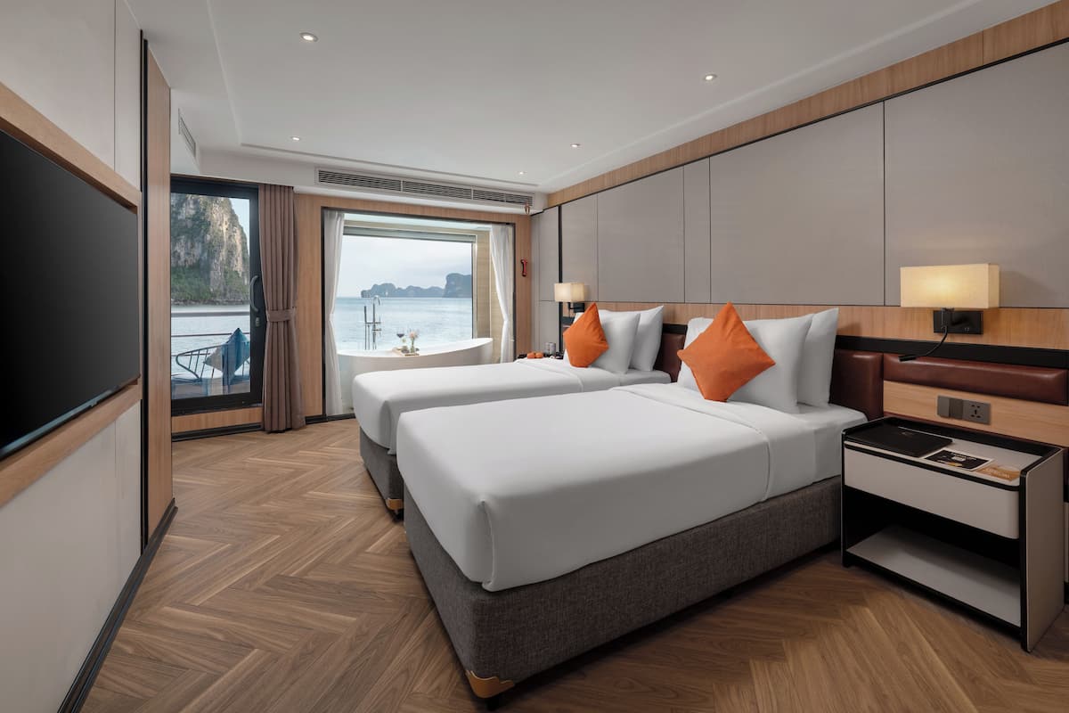Ett hotellrum med två sängar, en TV, ett nattduksbord och utsikt över havet.