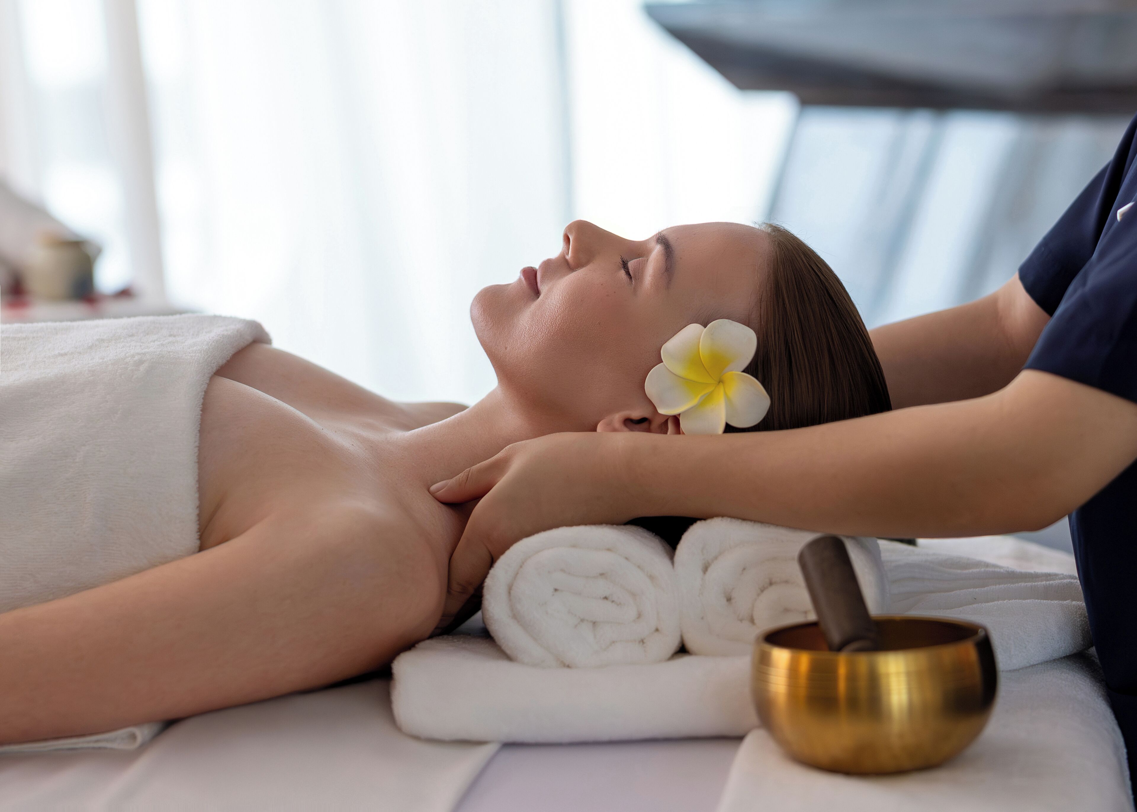A person receiving a massage with a flower and a golden bowl on the table.