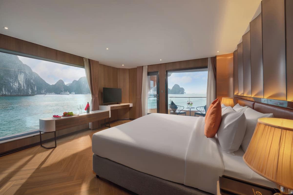 Ett modernt hotellrum med en stor säng, ett skrivbord, en TV och utsikt över havet.