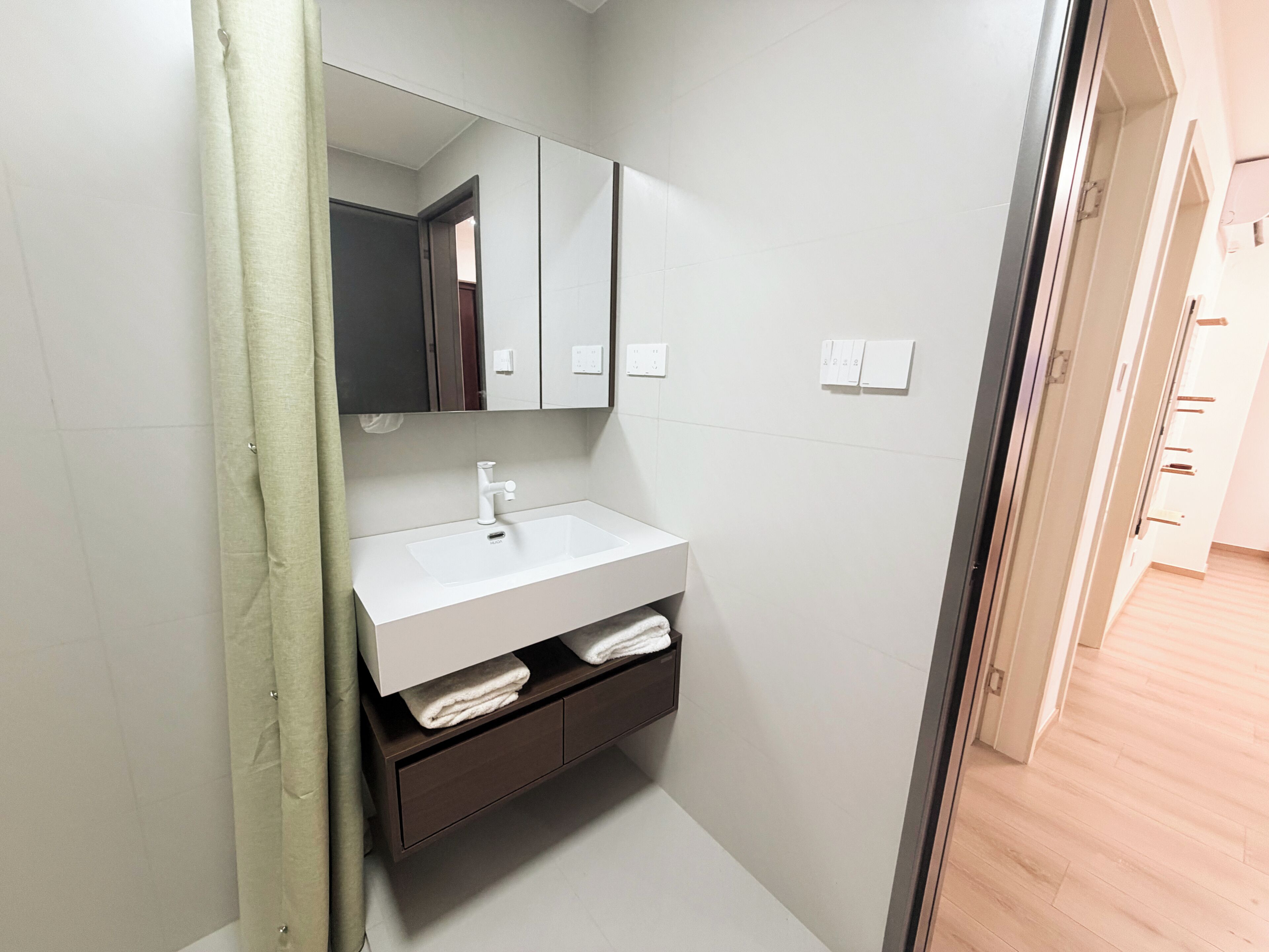 Un baño con lavamanos blanco, espejo y toallero.