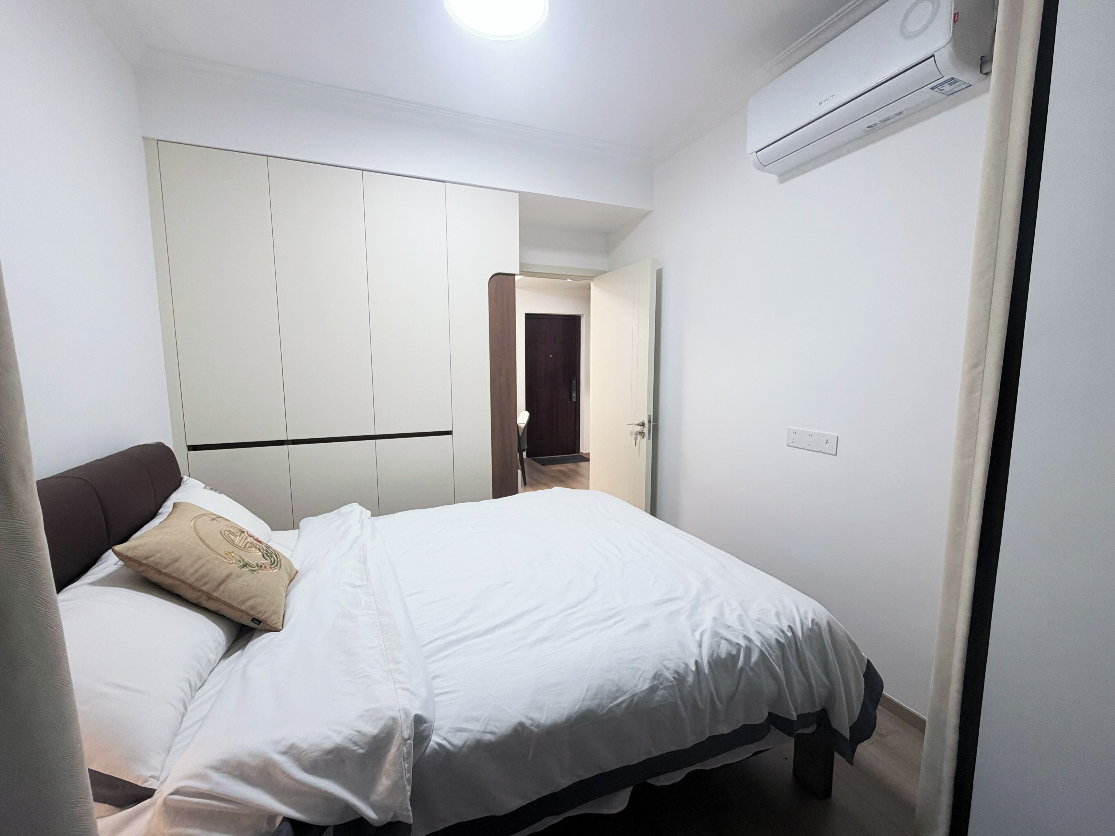 Une chambre à coucher comprenant un lit, une armoire, un appareil de climatisation et une porte donnant sur une autre pièce.