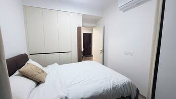 Une chambre à coucher comprenant un lit, une armoire, un appareil de climatisation et une porte donnant sur une autre pièce.