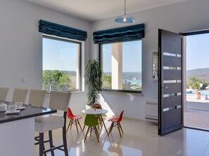 A modern dining area with a table and chairs, large windows with blue curtains, and a view of the outdoors. - Rachele by Interhome (Pula/Rakalj)