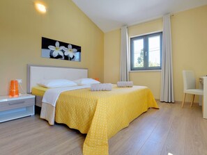 A bedroom with a bed, a nightstand, a chair, a window with curtains, and a wall-mounted picture. - Rachele by Interhome (Pula/Rakalj)